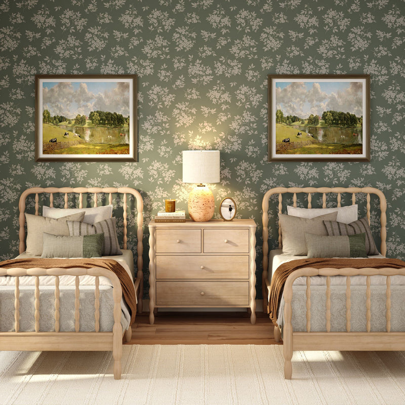 Cozy farmhouse twin bedroom with green floral wallpaper, light spindle beds, neutral bedding, nightstand with lamp and framed landscape art.