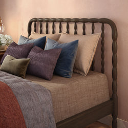 Wooden spindle bed frame with layered neutral linen bedding and velvet decorative pillows in a cozy blush bedroom interior.
