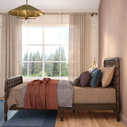 Cozy modern rustic bedroom with carved wooden bed frame, earth-toned bedding and textured pillows, sheer curtains and a large window framing a pine forest view.