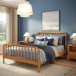 Coastal blue bedroom with spindle oak bed, layered navy and white bedding, wooden nightstands with lamps, ocean wall art, large window and hardwood floors