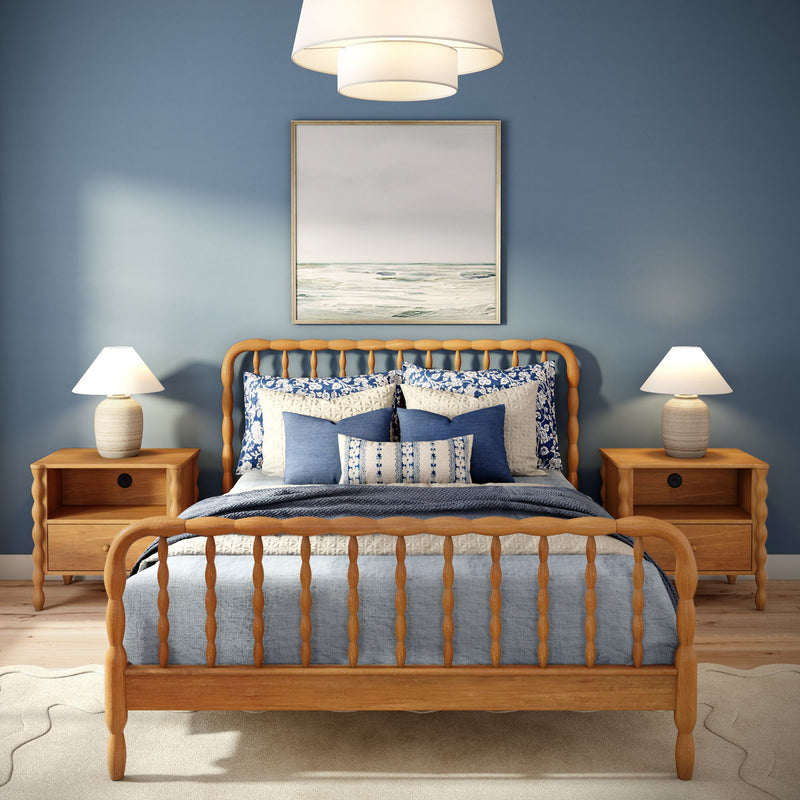 Coastal blue bedroom with wooden spindle bed, navy and white bedding, matching nightstands and lamps, and framed seascape wall art.