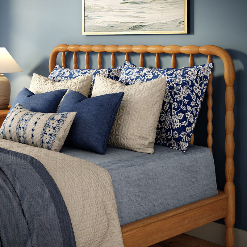 Wooden spindle bed with blue and beige quilt and patterned navy and cream decorative pillows in a cozy coastal farmhouse bedroom