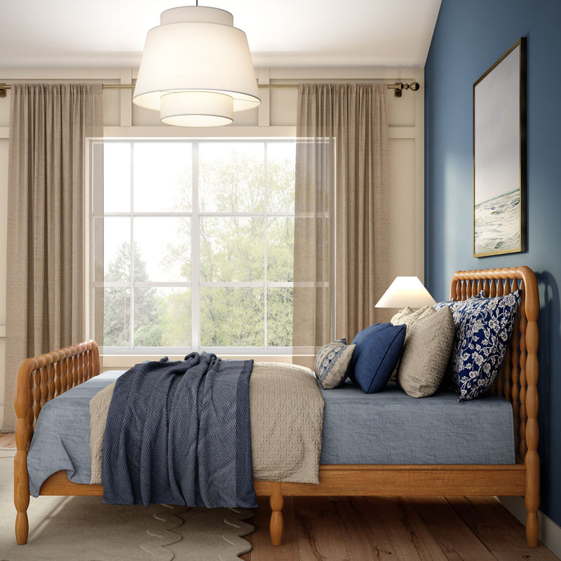 Cozy modern bedroom with wooden spindle bed, blue and beige bedding, patterned throw pillows, large window with neutral curtains and natural light