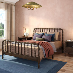Modern farmhouse bedroom with dark wooden spindle bed, layered neutral and rust bedding, blue area rug, peach textured wall.