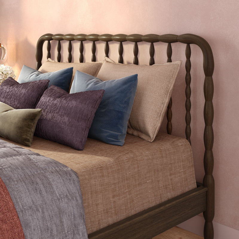 Cozy bedroom with dark wood spindle headboard, neutral linen bedding and textured velvet decorative pillows in purple, blue, and olive against a blush pink wall