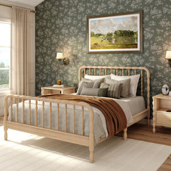 Cozy modern farmhouse bedroom interior with light wood spindle bed, green floral wallpaper, neutral layered bedding and brown throw, matching wood nightstands, wall sconces, framed landscape art and bright natural light