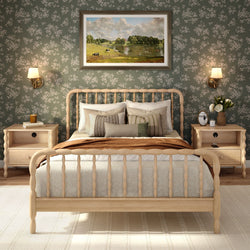 Cozy farmhouse bedroom with natural wood spindle bed, green floral wallpaper, neutral layered bedding, matching light-wood nightstands and wall sconces.