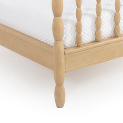 Close-up of light natural wood spindle bed frame leg and side rail with white quilted mattress, modern farmhouse bedroom furniture detail