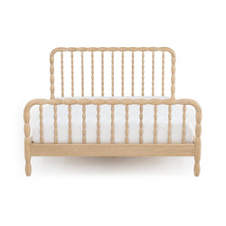 Front view of a natural light-wood spindle bed frame with turned posts, curved headboard and footboard, and white mattress — farmhouse-style wooden bed