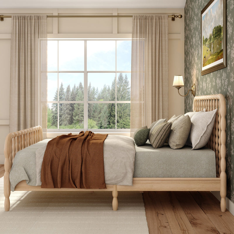 Cozy rustic bedroom with wooden spindle bed, neutral linens, rust knit throw, layered pillows and large window overlooking pine forest