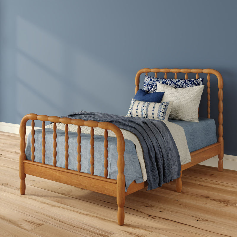 Wooden spindle bed with blue linen bedding, patterned decorative pillows and knit throw against a soft blue bedroom wall