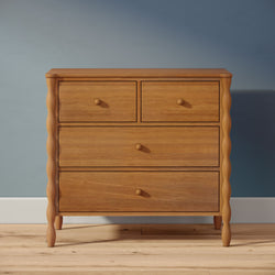 Solid oak wooden dresser with turned legs and four drawers, natural wood finish on hardwood floor against a blue wall