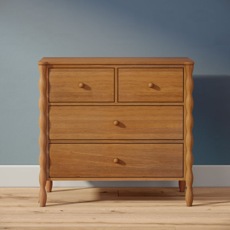 Solid oak wooden dresser with turned legs and four drawers, natural wood finish on hardwood floor against a blue wall