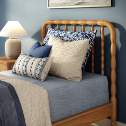Cozy bedroom close-up with wooden spindle headboard, blue and cream patterned pillows, blue bedding and bedside lamp