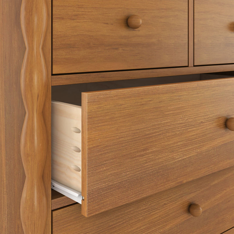 Close-up of a wooden bedroom dresser with a partially open drawer showing warm natural wood grain, round wooden knob, visible drawer joinery and metal slide