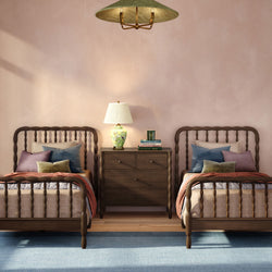 Cozy twin bedroom interior with wooden spindle beds, dark wood nightstand, floral ceramic table lamp, decorative throw pillows, pastel pink wall and soft blue rug
