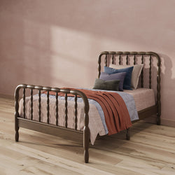 Cozy modern farmhouse bedroom with dark wooden spindle bed, layered textured bedding and pillows, rust knit throw, blush plaster wall and oak hardwood floor