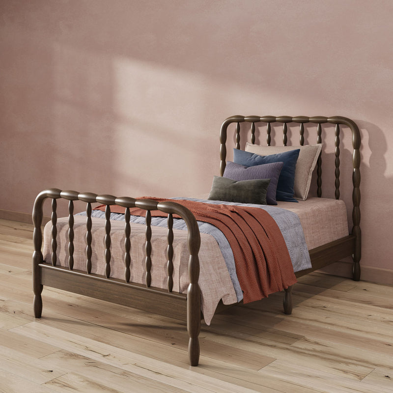 Cozy modern farmhouse bedroom with dark wooden spindle bed, layered textured bedding and pillows, rust knit throw, blush plaster wall and oak hardwood floor