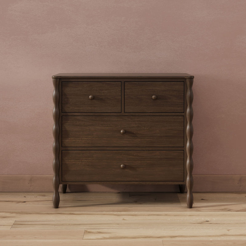 Dark walnut wooden dresser with turned legs and drawers against a dusty pink textured wall on light hardwood floor, minimalist bedroom furniture