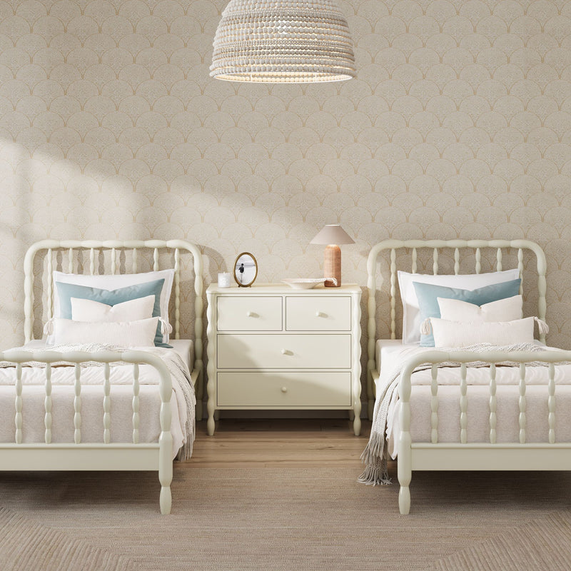 Neutral twin bedroom with cream spindle beds, beige scallop-pattern wallpaper, cream nightstand with lamp and oval mirror, woven beaded pendant light and soft blue accent pillows