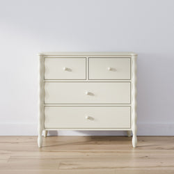 Cream wooden chest of drawers dresser with round knobs on light hardwood floor against a white wall, minimalist bedroom storage furniture