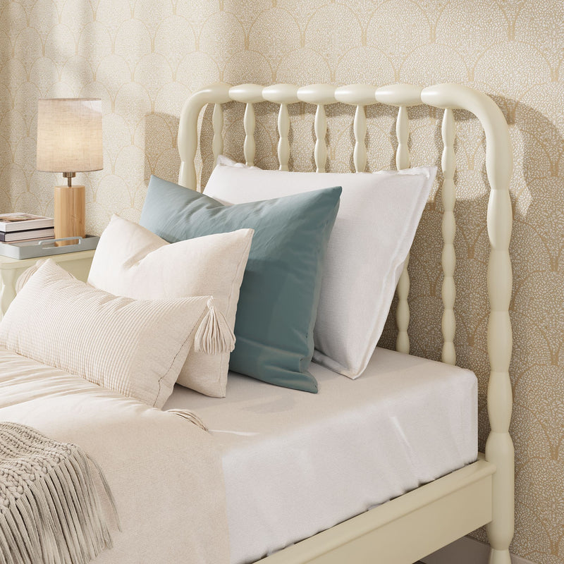 Cozy neutral bedroom with cream spindle headboard, layered beige and teal pillows, wooden bedside lamp and textured scallop-pattern wallpaper