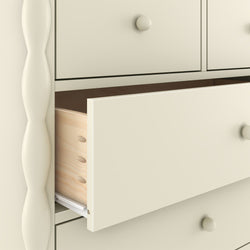 Close-up of a cream-painted wooden dresser with a partially open drawer revealing dovetail joints, round knob and turned leg detail — bedroom storage furniture