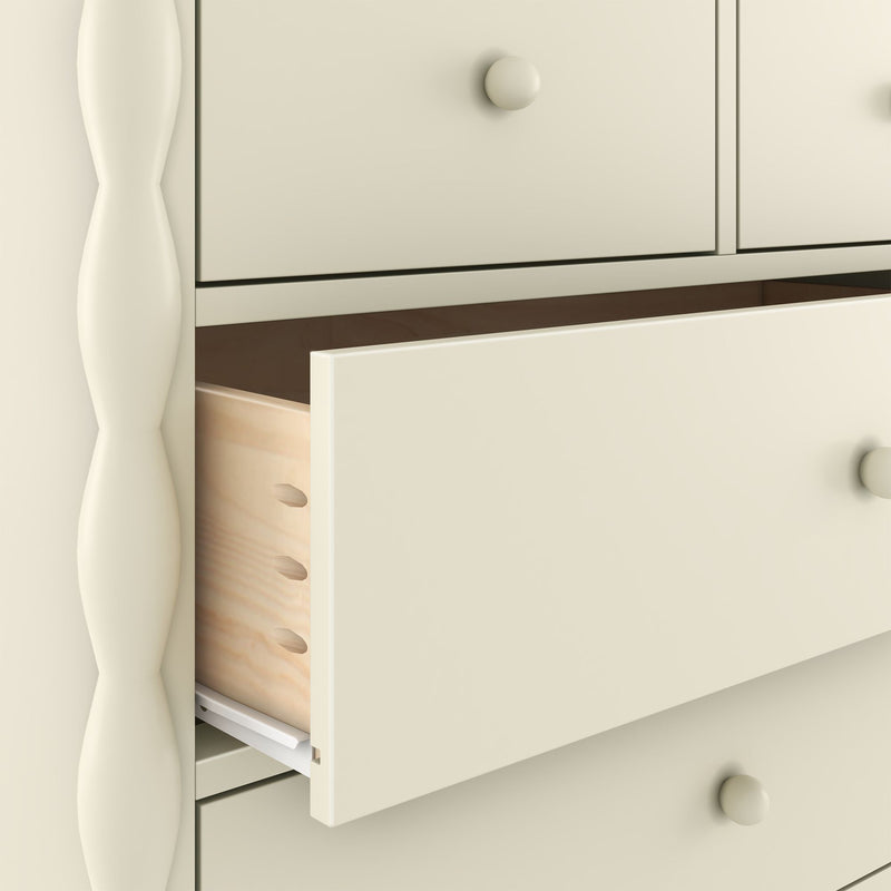 Close-up of a cream-painted wooden dresser with a partially open drawer revealing dovetail joints, round knob and turned leg detail — bedroom storage furniture