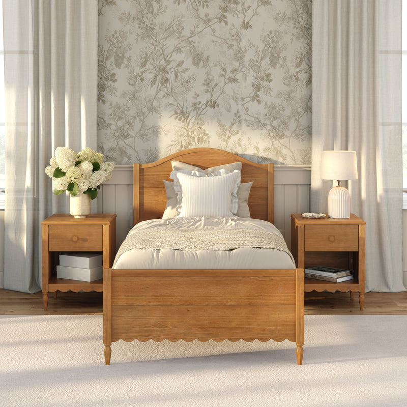 Cozy farmhouse bedroom with wooden bed frame and matching nightstands, neutral bedding, floral wallpaper, table lamp and white hydrangea bouquet in natural light