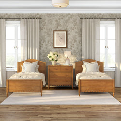 Cozy farmhouse-style twin bedroom interior with matching wooden beds, central wooden dresser, neutral floral wallpaper, white curtains, bedside lamp and vase of white hydrangeas.