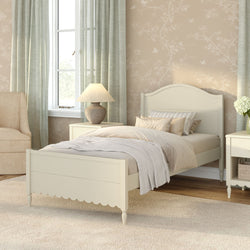 Cozy neutral farmhouse bedroom with cream wooden twin bed, beige layered bedding, floral wallpaper, nightstand lamp and pale green curtains