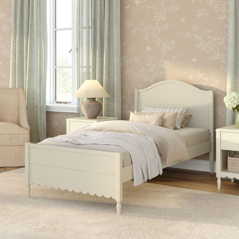 Cozy neutral farmhouse bedroom with cream wooden twin bed, beige layered bedding, floral wallpaper, nightstand lamp and pale green curtains