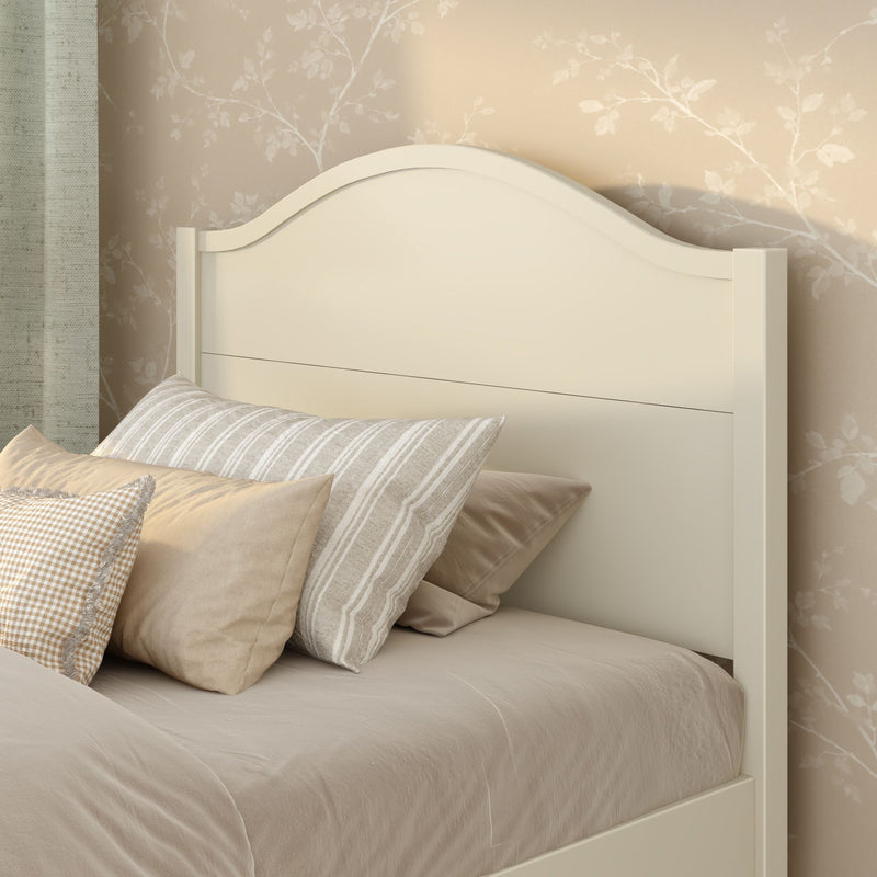 Cream curved wooden headboard with neutral beige bedding and striped and gingham pillows against beige floral wallpaper, cozy farmhouse bedroom decor