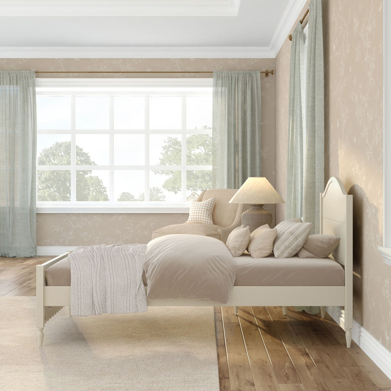 Neutral beige bedroom interior with cream twin bed, layered bedding and knit throw, upholstered accent chair, table lamp, large grid window with sheer green curtains and hardwood floor
