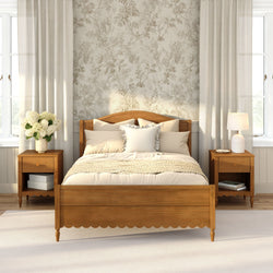 Cozy farmhouse bedroom with wooden bed frame, neutral bedding and throw, floral wallpaper, matching nightstands, lamp, white hydrangea vase and soft natural light