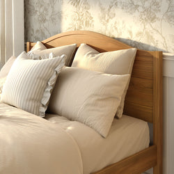 Wooden bed frame with beige linen duvet and pillows, striped ruffle accent pillow, and floral wallpaper for a cozy neutral farmhouse bedroom decor