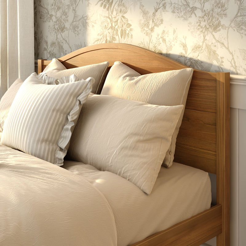 Wooden bed frame with beige linen duvet and pillows, striped ruffle accent pillow, and floral wallpaper for a cozy neutral farmhouse bedroom decor