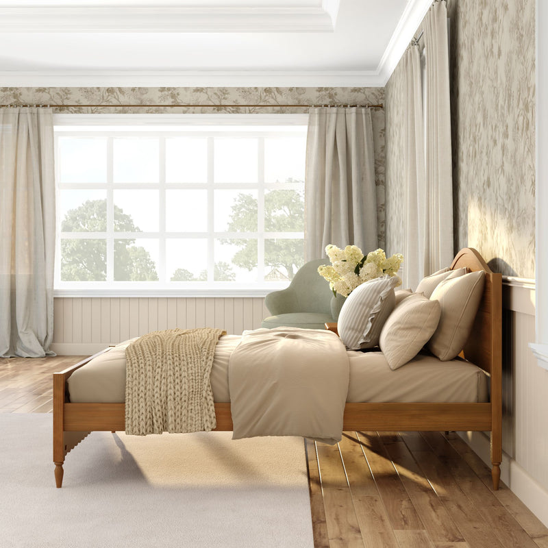 Sunlit neutral bedroom with wooden bed frame, beige linens and chunky knit throw, large grid window, pale curtains, green accent chair and vase of white flowers, modern farmhouse style
