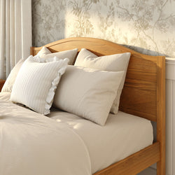Cozy bedroom with wooden headboard, neutral beige bedding and pillows, floral wallpaper and soft natural light