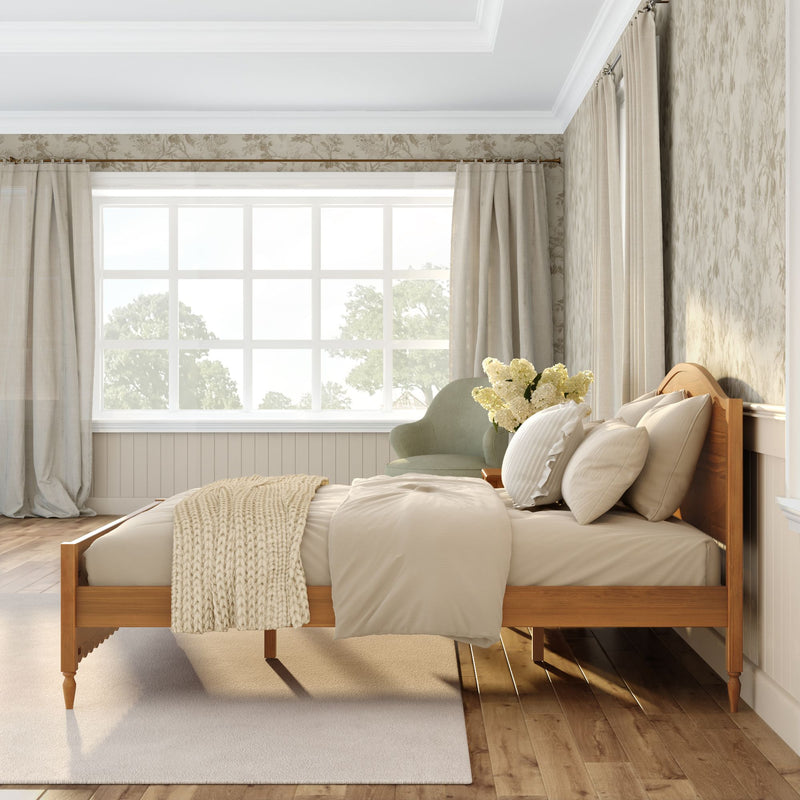 Bright cozy neutral bedroom with wooden bed frame, beige linen bedding, chunky knit throw, green accent chair, textured wallpaper and large sunlit window