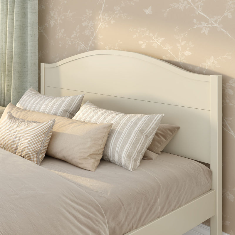 Cozy neutral bedroom interior with cream wooden headboard, beige linen bedding and striped throw pillows against floral wallpaper and sage green curtains