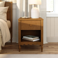 Wooden bedside table with white ribbed ceramic lamp and decorative dish beside beige bed in a cozy modern farmhouse bedroom