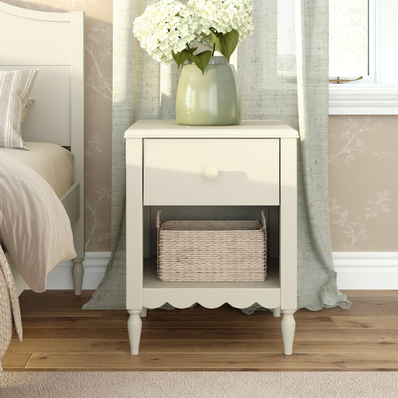 Cream bedside table nightstand with drawer and wicker basket, green ceramic vase holding white hydrangeas in neutral bedroom decor