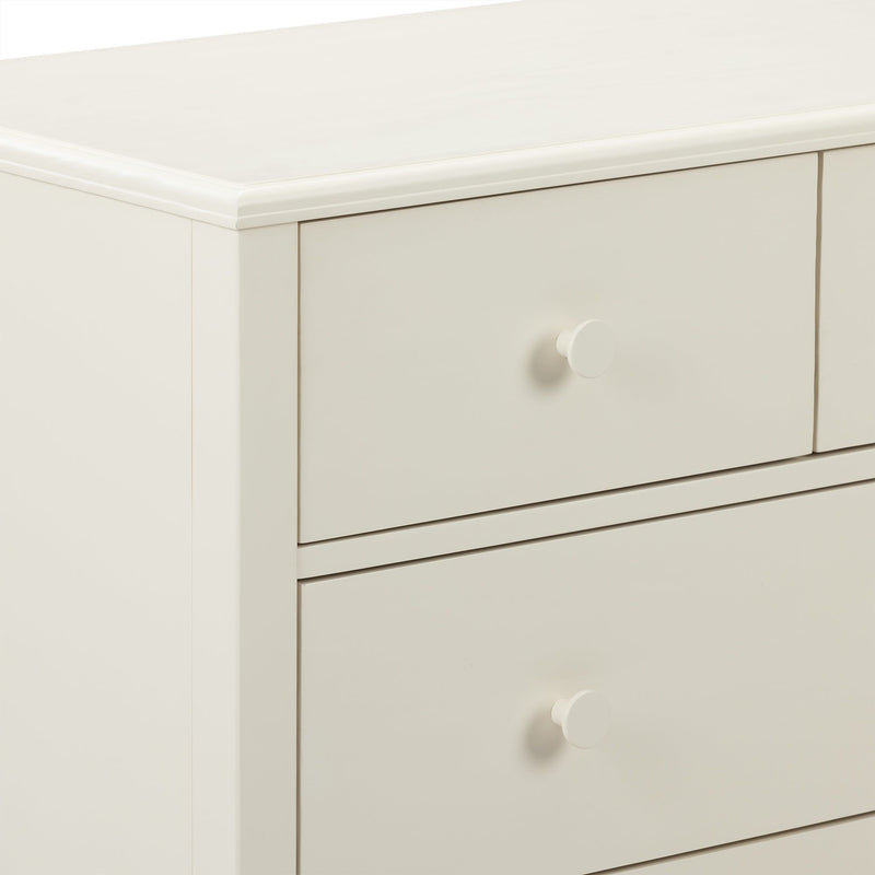 Close-up of cream white wooden dresser drawers with round knob and smooth beveled top, modern nursery bedroom storage cabinet