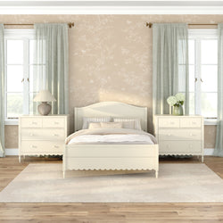Neutral master bedroom with cream wooden bed and matching dressers, sheer sage curtains, beige floral wallpaper, area rug on hardwood floors, lamp and hydrangea vase