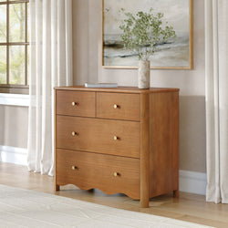 Mid-century modern wooden dresser with brass knobs, marble vase of greenery and framed coastal art in a neutral bedroom with soft natural light