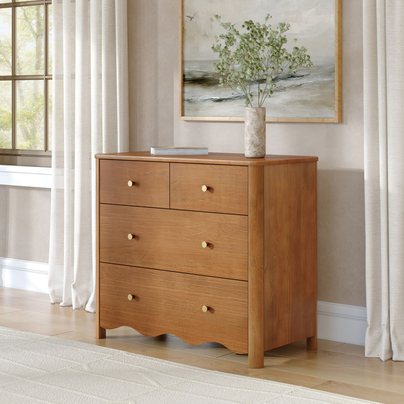 Mid-century modern wooden dresser with brass knobs, marble vase of greenery and framed coastal art in a neutral bedroom with soft natural light