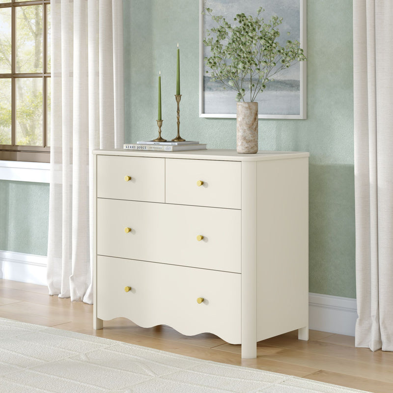 Cream wooden dresser with gold knobs under a mint green textured wall, marble vase with greenery and two green taper candles beside a sunlit window with sheer curtains — modern bedroom decor