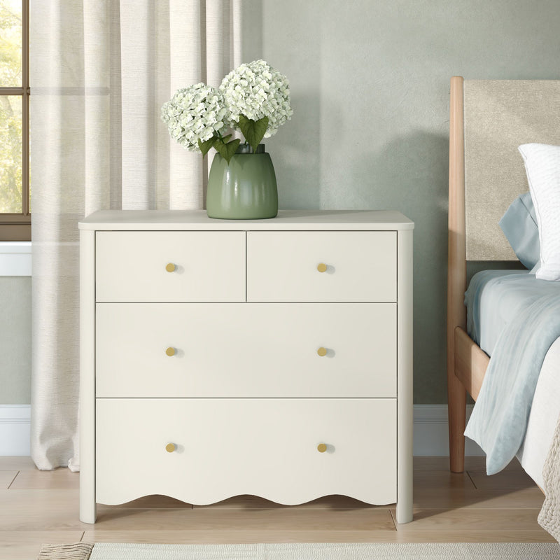 White hydrangea bouquet in a green ceramic vase on a cream dresser nightstand in a neutral modern bedroom with beige curtains