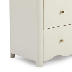 Close-up of cream-painted wooden dresser drawers with brass cone knobs and scalloped base, modern minimalist bedroom nightstand storage